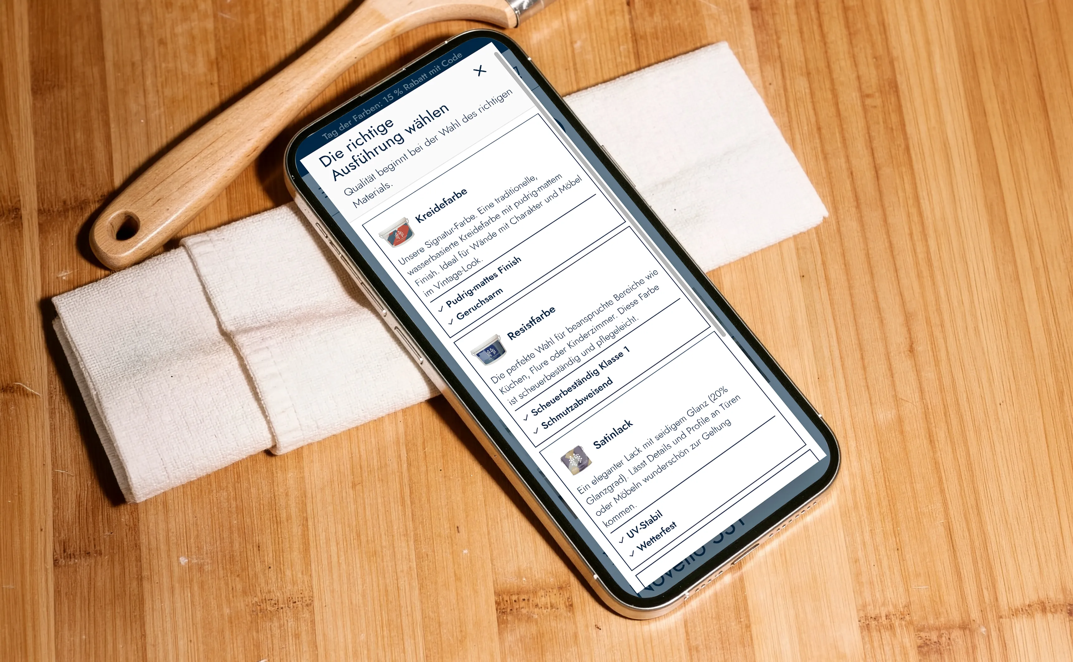 Anna-von-Mangoldt-Website mit Farbauswahl auf einem Smartphone neben einem Pinsel
