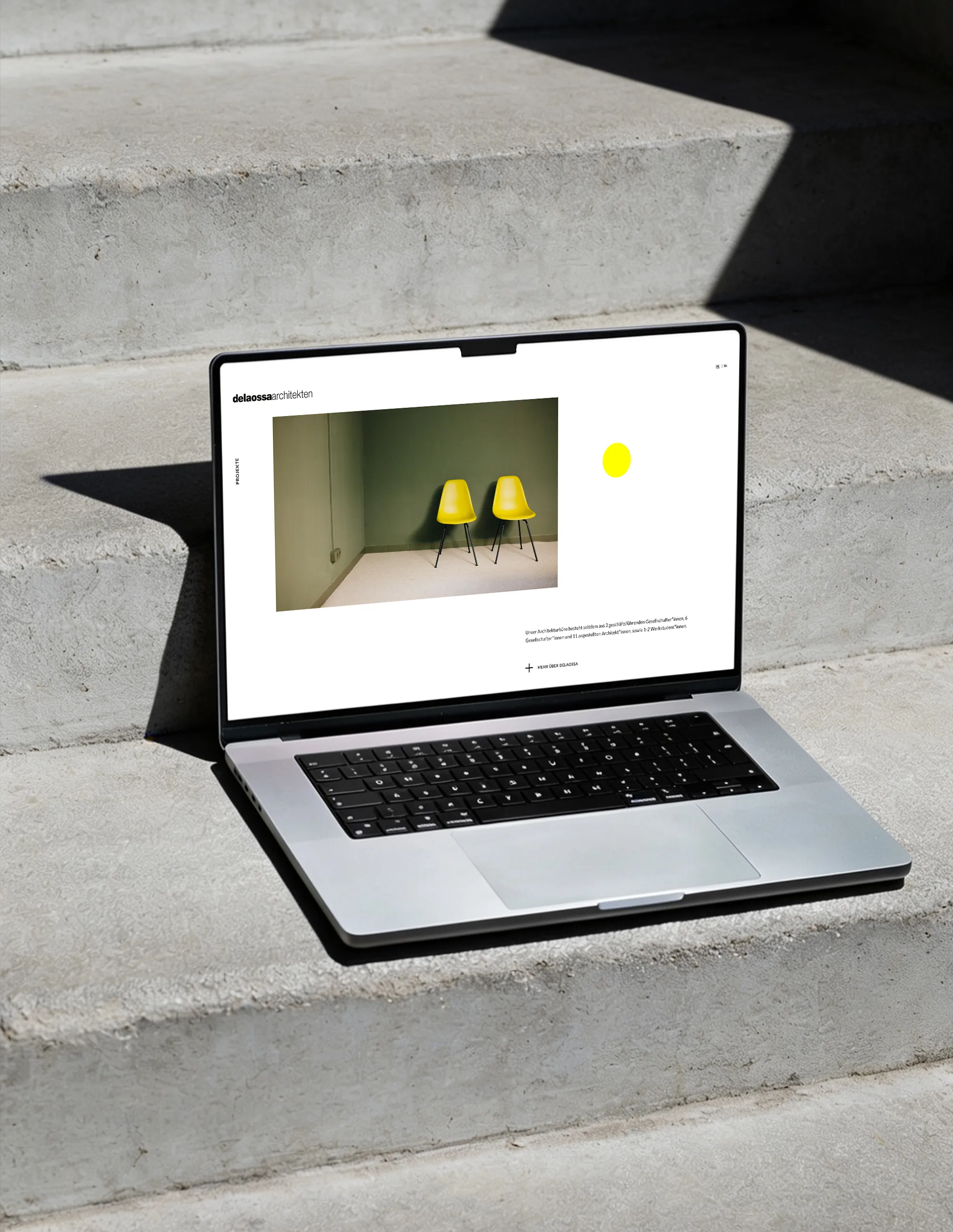 Laptop mit der Website von delaossa architekten, im Hintergrund eine Betontreppe
